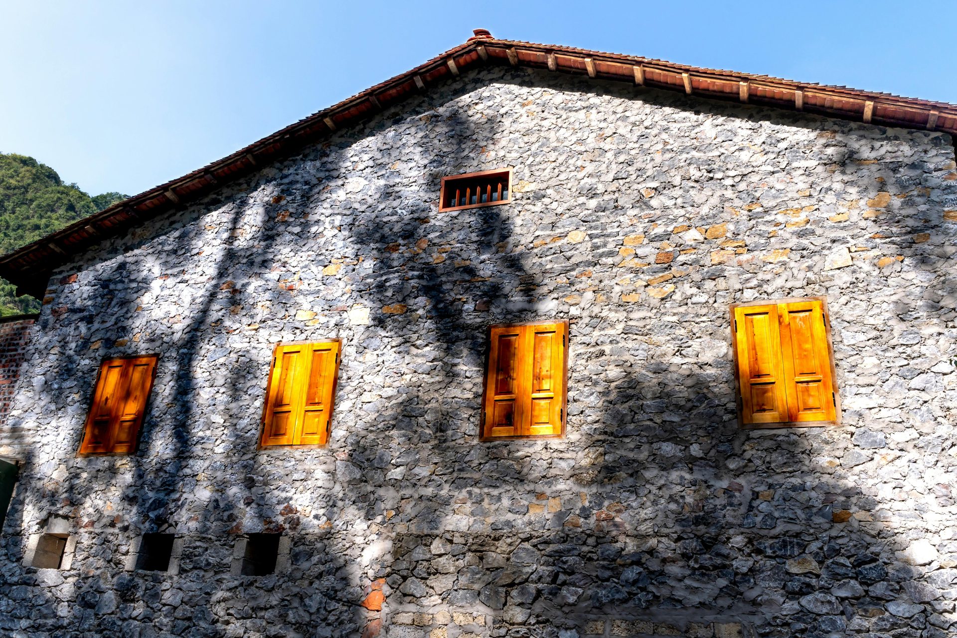 Encantadora casa rústica de piedra con contraventanas de madera de colores vivos bajo un cielo azul brillante.