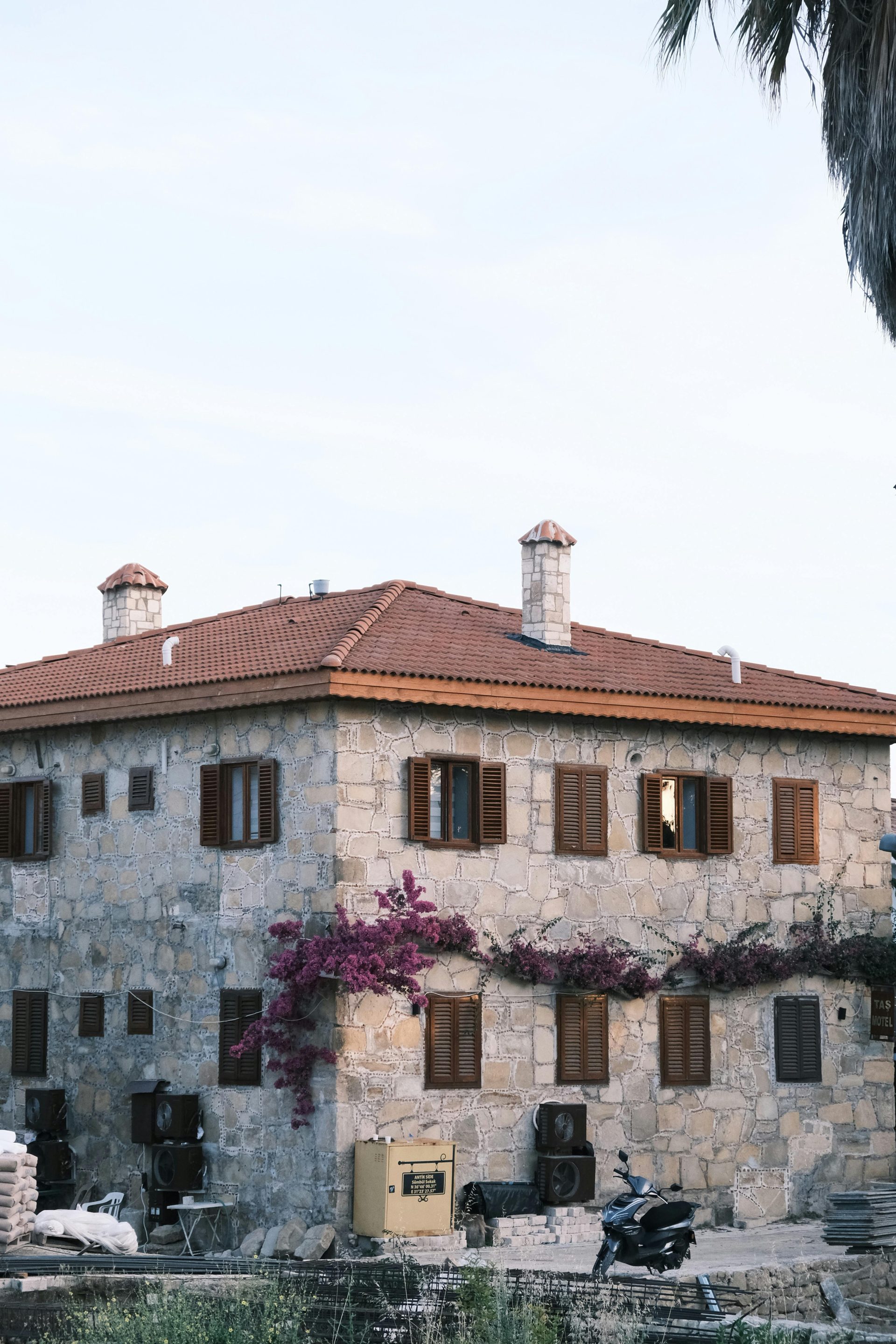 Charming stone house in Antalya, Türkiye, adorned with blooming purple flowers and rustic shutters.