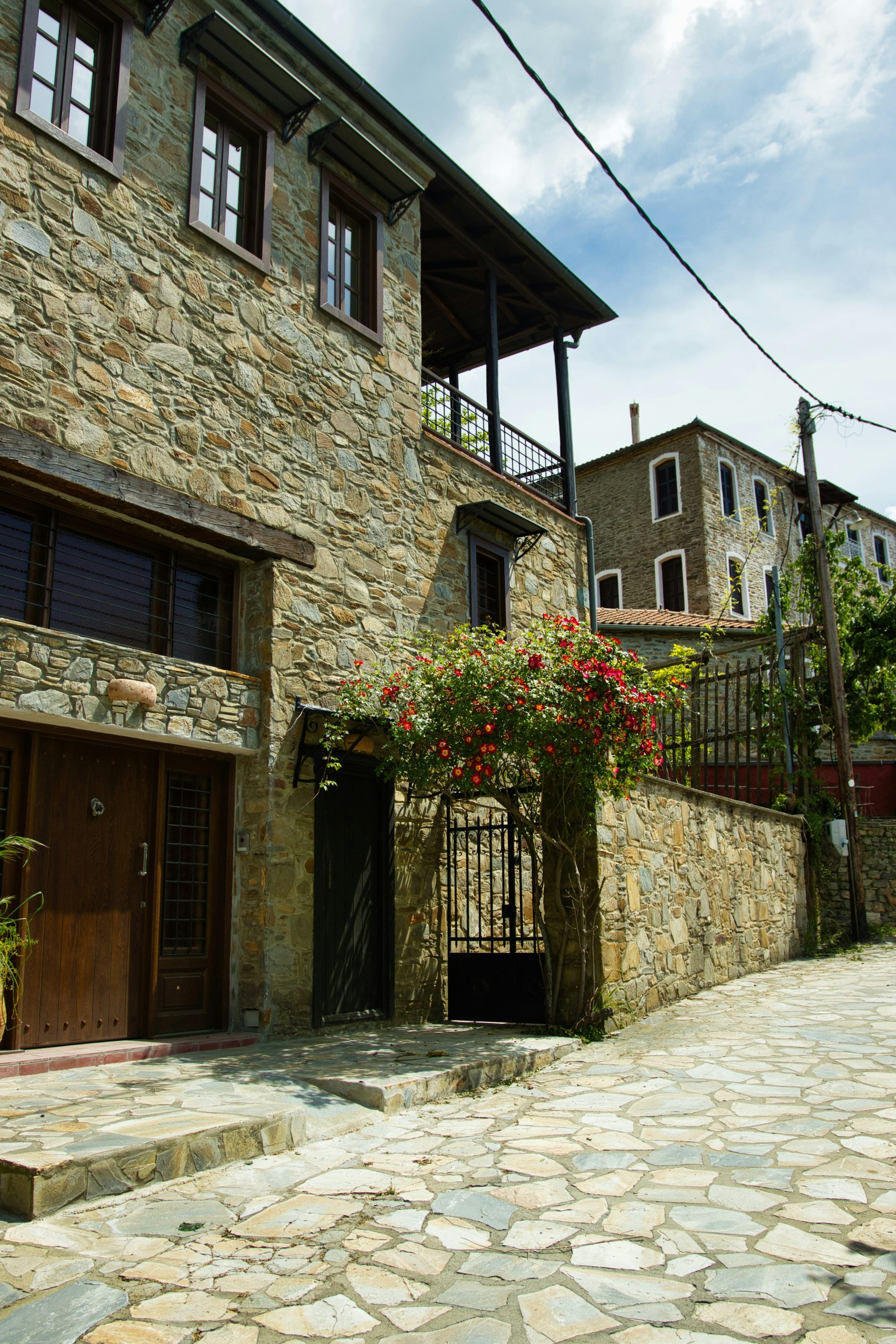 Edificios de piedra bordean una calle empedrada cubierta de enredaderas en flor.